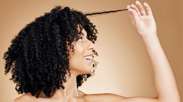 Mulher negra sorridente com o cabelo cacheado considera fazer um dos tipos de franja em cabelo cacheado.
