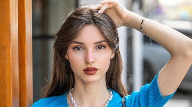 Jovem posa tocando para destacar seu com o cabelo liso e franja cortina