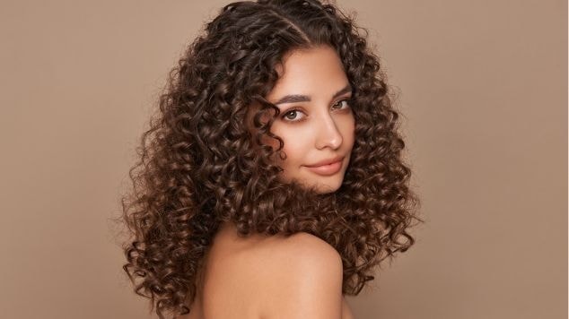 Jovem com um leve sorriso e um corte de cabelo cacheado em seus cachos