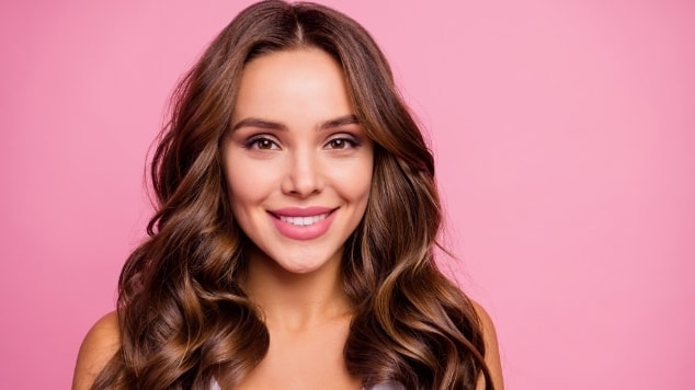 Modelo de cabelo longo e preto com uma parte lisa e uma parte ondulada, durante a transição capilar ondulada, em fundo cinza.